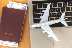 passaportes e dinheiro perto de computador portátil e avião na mesa. conceito de reserva de bilhetes online foto