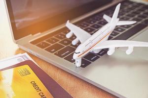 passagens aéreas, passaportes e cartão de crédito perto de computador portátil e avião na mesa. conceito de reserva de bilhetes online foto