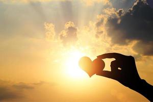 mão de silhueta segurando coração contra a luz do sol - conceito de amor - sozinho - solitário foto