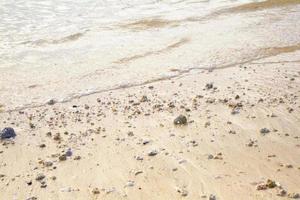 areia de praia estética com pequenas pedras e água do mar clara foto