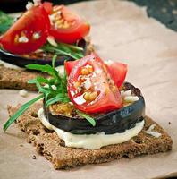 sanduíches de pão estaladiço de dieta vegetariana com queijo creme de alho, berinjela assada, rúcula e tomate cereja em fundo de madeira velho foto
