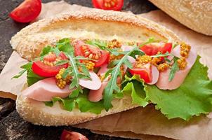 sanduíche com linguiça, alface, tomate e rúcula no fundo de madeira velho foto