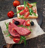 sanduíche com salsicha, azeitona, tomate e rúcula no antigo fundo de madeira foto