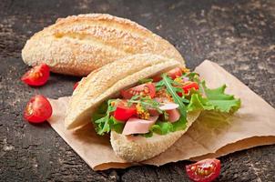 sanduíche com linguiça, alface, tomate e rúcula no fundo de madeira velho foto