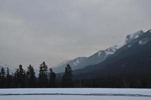 montanhas rochosas cobertas de neve com lago congelado em primeiro plano foto