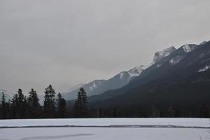 montanhas rochosas cobertas de neve com lago congelado em primeiro plano foto