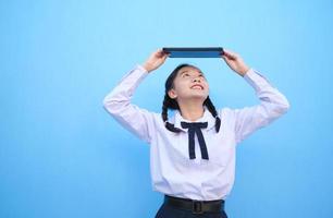 menina da escola segurando o tablet sobre fundo azul. foto