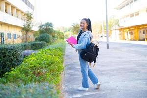 aluna feliz segura livro e mochila na escola, menina asiática. foto