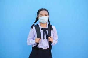 menina da escola usa máscara em fundo azul, de volta à escola. foto