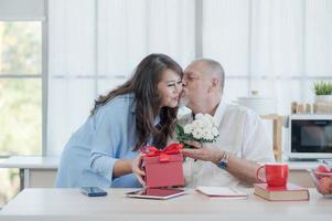 um casal europeu idoso e uma mulher asiática alegremente dão um ao outro caixas de presente e flores por ocasião do dia dos namorados foto