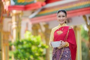 uma bela mulher tailandesa de vestido tailandês com ornamentos de ouro segura um copo de água para o festival songkran ou ano novo tailandês foto