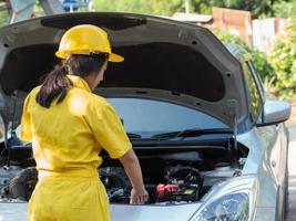 a mulher de uniforme do mecânico está abrindo a tampa do radiador do motor para verificar o nível da água foto