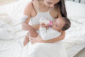 uma linda mulher asiática, carregando seu bebê recém-nascido com amor e carinho, e alimentando-a com felicidade foto