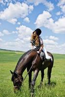 menina bonita andando a cavalo em um campo em dia ensolarado. foto