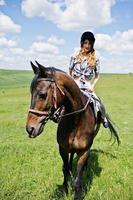 menina bonita andando a cavalo em um campo em dia ensolarado. foto