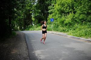 garota esportiva no sportswear correndo em um parque verde e treinando na natureza. um estilo de vida saudável. foto