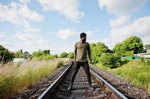 legal negro afro-americano em óculos de sol andando e posando na ferrovia na zona rural. foto