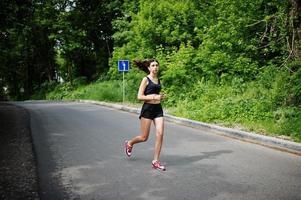 garota esportiva no sportswear correndo em um parque verde e treinando na natureza. um estilo de vida saudável. foto