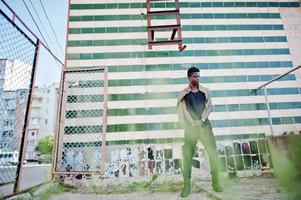 Afro-americano jovem atraente em roupas casuais em pé ao lado da parede de azulejos. foto