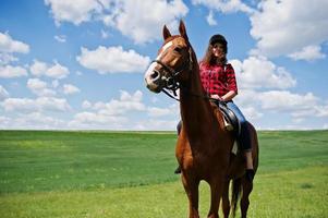 menina bonita andando a cavalo em um campo em dia ensolarado. foto