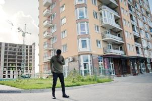 homem afro-americano bonito e atraente posando ao lado do prédio alto em uma rua. foto