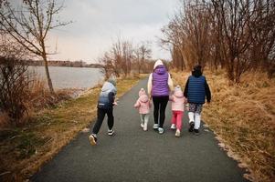 costas da mãe andando com crianças no caminho à beira do lago. foto