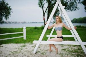 retrato de um modelo feminino atraente posando ao lado da construção de madeira branca triangular no parque com um lago ao fundo. foto