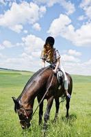 menina bonita andando a cavalo em um campo em dia ensolarado. foto