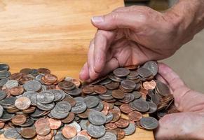 mãos pegando troco solto dos eua com moedas mistas na mesa de madeira foto