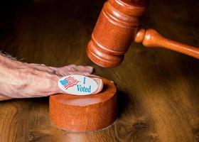 votei no botão de campanha ou adesivo na mão com um martelo e um martelo para ilustrar processos judiciais sobre votação foto
