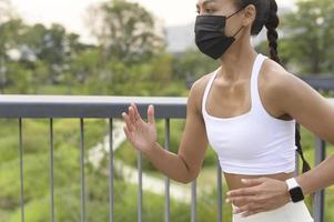 jovem fitness em roupas esportivas usando máscara facial enquanto se exercita no parque da cidade, saúde e estilos de vida. foto