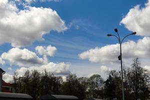 lindo céu azul com enormes nuvens brancas sobre a paisagem urbana com lâmpada de rua foto