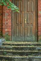 velha porta de madeira marrom no prédio de parede de tijolo vermelho com escadas verdes resistidas foto