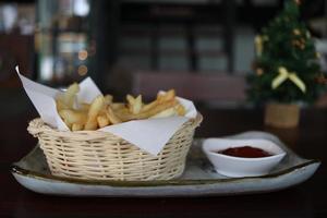 batatas fritas na cesta e molho de tomate no copo branco estão no prato e fundo de madeira. foto