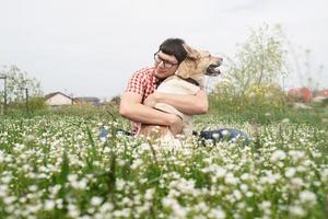 homem feliz sentado com cão pastor de raça mista na grama verde em flores da primavera foto