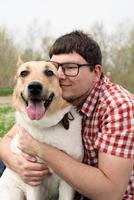 homem feliz sentado com cão pastor de raça mista na grama verde em flores da primavera foto