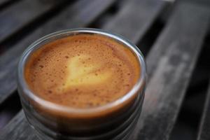 feche a foto de um copo de café com uma mistura de café expresso e suco de laranja, mostrando espuma brilhante com fundo desfocado.