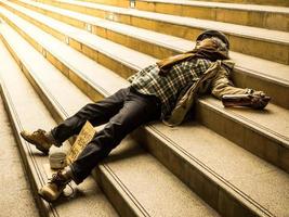 um pobre sem-teto dorme em uma escada com uma conta de doação