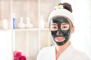 uma linda mulher asiática tem uma máscara facial usando a lama do spa para tratamento facial em uma loja de spa foto