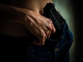 mãos de jovem com arma em seu jeans azul foto