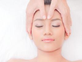 uma linda mulher asiática fecha os olhos, relaxa em uma loja de spa com uma massagem facial de um massagista profissional foto