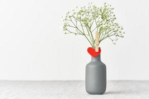 Dia dos namorados. delicadas flores brancas em um vaso. coração de feltro vermelho - símbolo dos amantes. foto