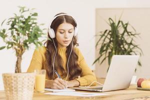 mulher feliz em fones de ouvido sem fio estudando curso online, usando pc e escrevendo no bloco de notas foto