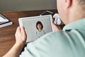 homem olha para tablet, videochamada para médico, comunicação com médico online. telemedicina foto