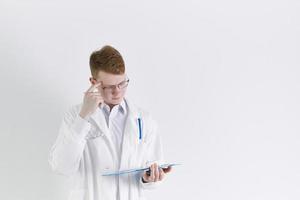 jovem estagiário médico estagiário fica em fundo branco. homem ruivo bonito, pensando foto