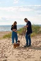 jovem casal feliz e cachorro andando na praia. mulher brincando com animal de estimação por brinquedo. foto