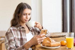 mulher visualizando redes sociais usando o celular, desfrutando de um café da manhã saudável. foto