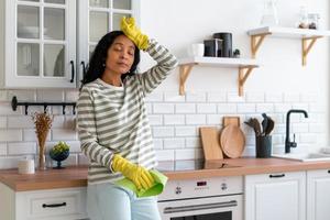 mulher afro-americana terminou de limpar a cozinha. cansado de lidar com poeira. conceito de trabalho doméstico foto