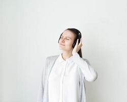 jovem fêmea está ouvindo música com fones de ouvido, garota em frente a parede cinza claro foto