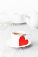 Dia dos Namorados. café da manhã para dois com chá e flores. coração de feltro vermelho é símbolo dos amantes foto